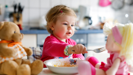 child pretending to feed her food to a doll for intuitive eating principle of offering a variety of foods