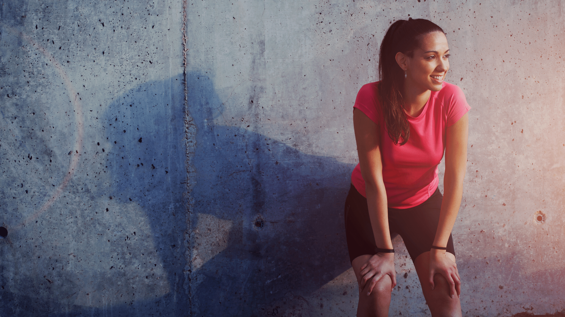 woman resting against wall and smiling after running