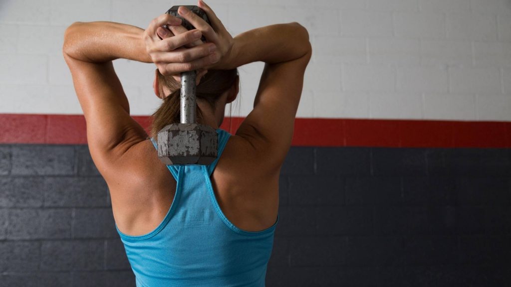 woman doing tricep exercise with dumbbell debunking does muscle burn fat