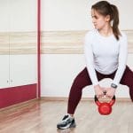 woman doing kettle bell exercise in front of gym mirror